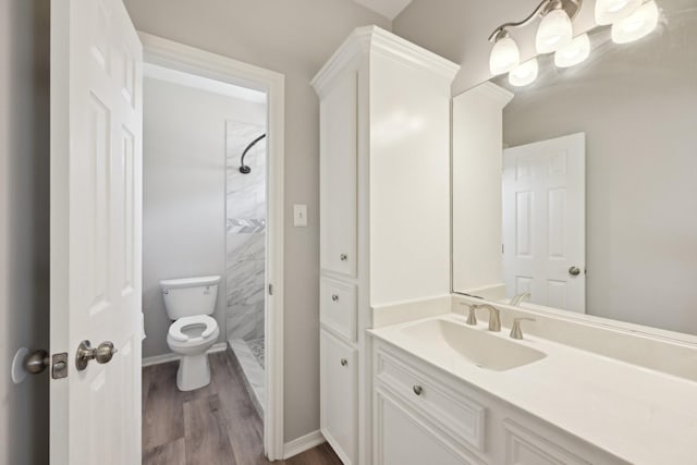 bathroom with wood finished floors, a shower stall, toilet, vanity, and baseboards