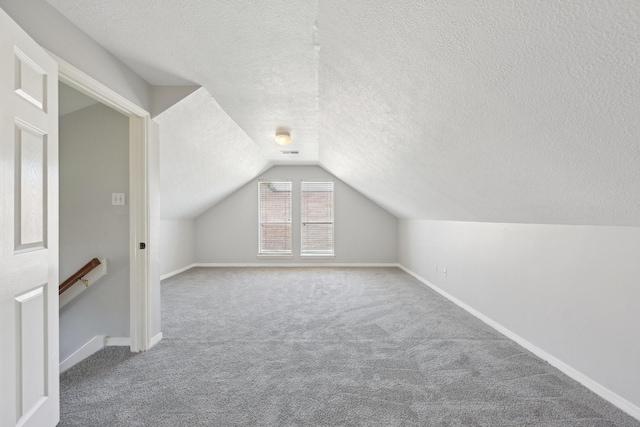 additional living space featuring a textured ceiling, baseboards, vaulted ceiling, and carpet floors