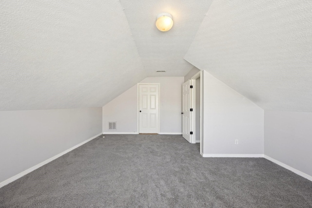 bonus room with vaulted ceiling, baseboards, visible vents, dark carpet, and a textured ceiling