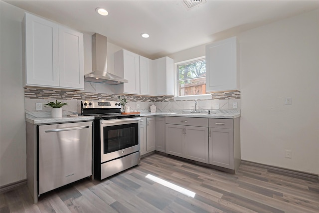 kitchen with light countertops, a sink, backsplash, appliances with stainless steel finishes, and wall chimney range hood