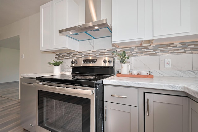 kitchen featuring white cabinetry, stainless steel electric stove, backsplash, wall chimney range hood, and wood finished floors