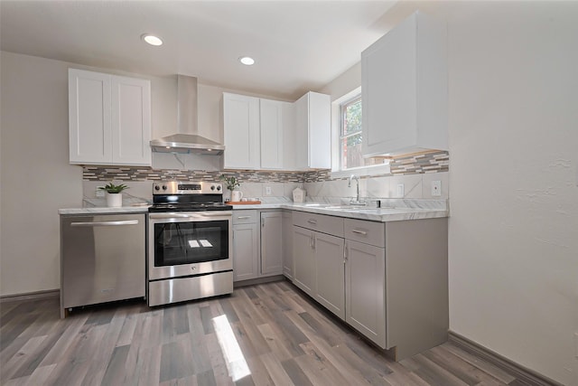 kitchen with light countertops, wall chimney exhaust hood, appliances with stainless steel finishes, a sink, and gray cabinets
