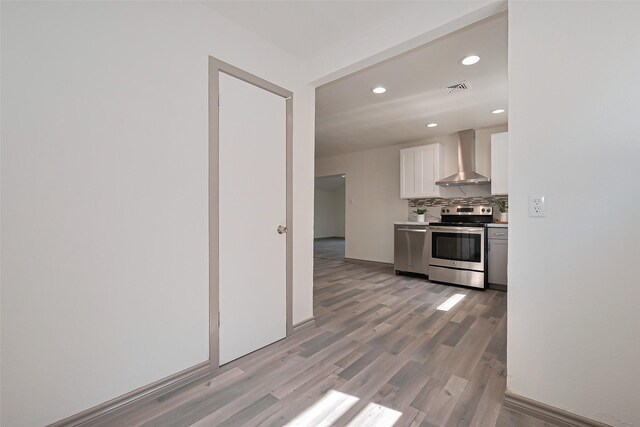 kitchen featuring light wood finished floors, white cabinetry, stainless steel appliances, wall chimney range hood, and visible vents