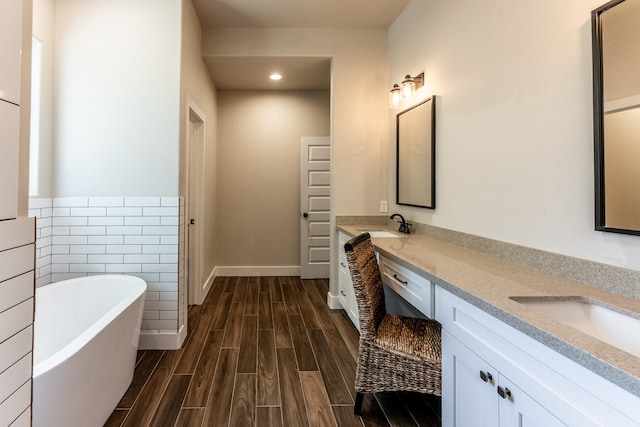 full bath with a sink, double vanity, recessed lighting, a freestanding tub, and wood finished floors