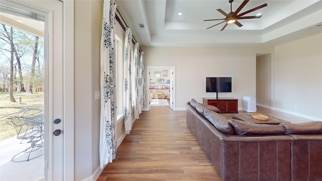 living area with ceiling fan, visible vents, wood finished floors, baseboards, and a tray ceiling