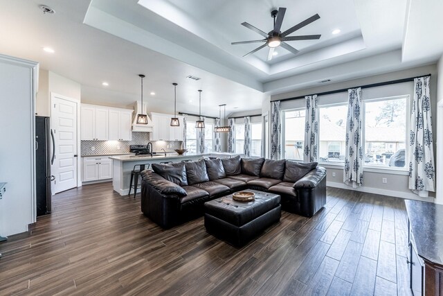 living area with recessed lighting, a ceiling fan, a tray ceiling, and dark wood-style floors
