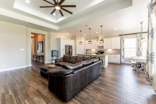 living room with recessed lighting, ceiling fan, dark wood finished floors, and a tray ceiling