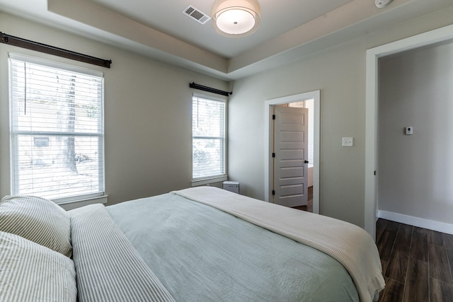 bedroom featuring visible vents, a raised ceiling, dark wood-style flooring, and baseboards