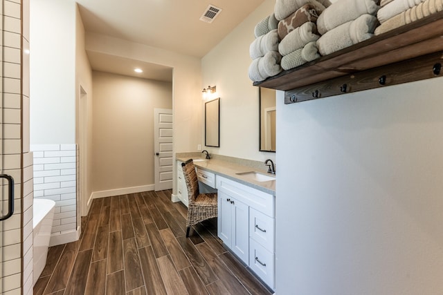 bathroom with a freestanding bath, a sink, recessed lighting, wood finished floors, and visible vents