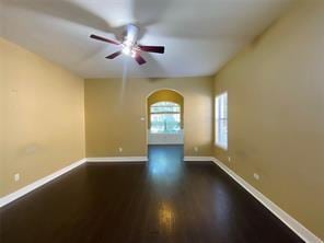 14959 Royal Birkdale St, Houston, TX 77095 - empty room featuring arched walkways, dark wood-style floors, ceiling fan, and baseboards