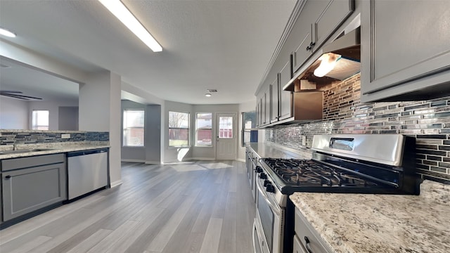 kitchen featuring light stone counters, decorative backsplash, stainless steel appliances, light wood-type flooring, and gray cabinets