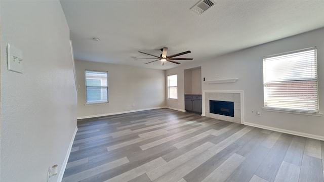 unfurnished living room with visible vents, baseboards, wood finished floors, a tiled fireplace, and a ceiling fan