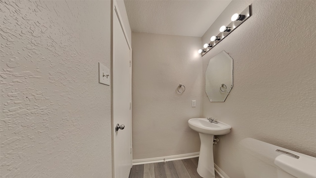 half bath featuring baseboards, wood finished floors, toilet, and a sink
