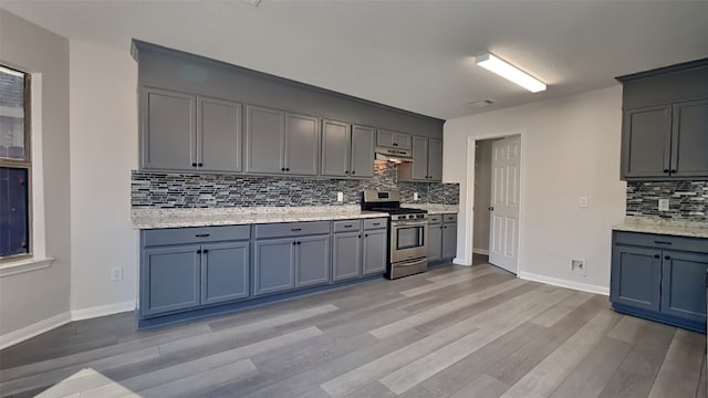 kitchen with tasteful backsplash, baseboards, under cabinet range hood, light wood-type flooring, and gas stove