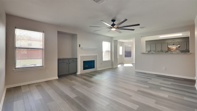 unfurnished living room with ceiling fan, visible vents, baseboards, light wood finished floors, and a fireplace