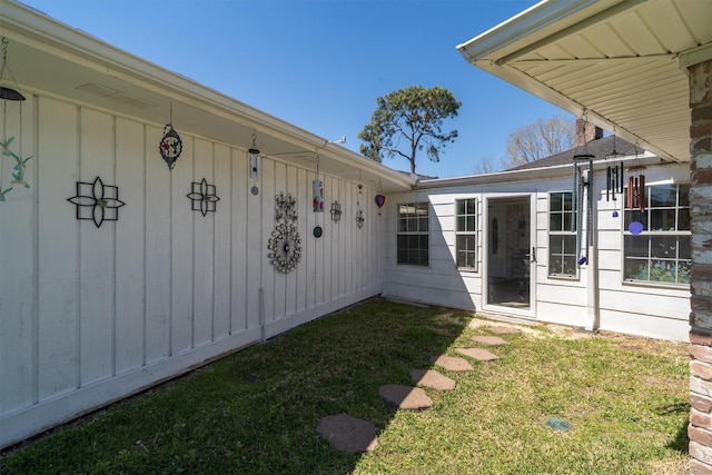 view of exterior entry with board and batten siding and a yard