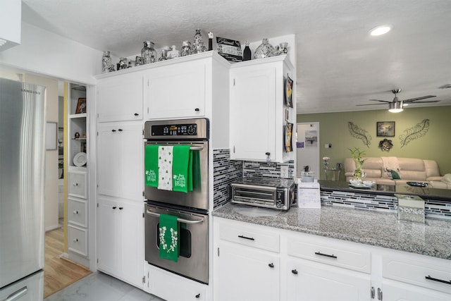 kitchen featuring open floor plan, white cabinets, light stone countertops, ceiling fan, and appliances with stainless steel finishes