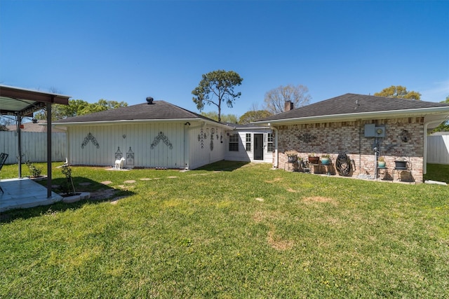 rear view of house featuring brick siding, fence, a chimney, and a lawn