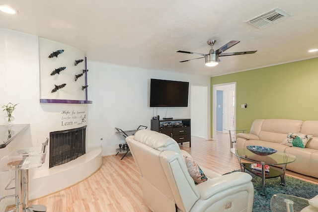 living area with a ceiling fan, a fireplace, visible vents, and wood finished floors