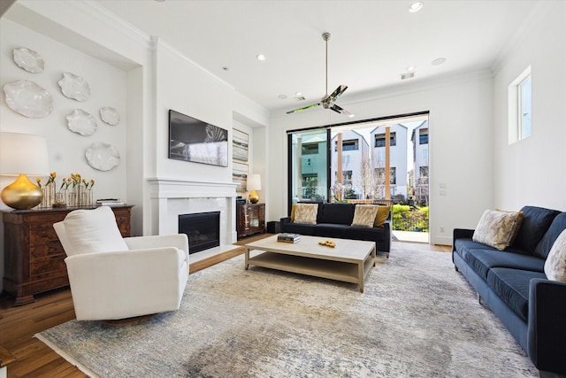 living area featuring a fireplace with flush hearth, visible vents, crown molding, and wood finished floors