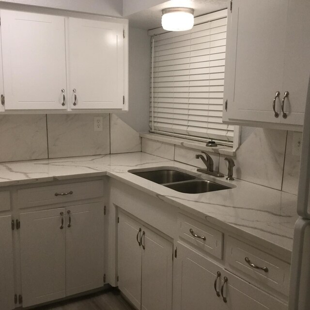 kitchen with light stone countertops, decorative backsplash, a sink, and white cabinets