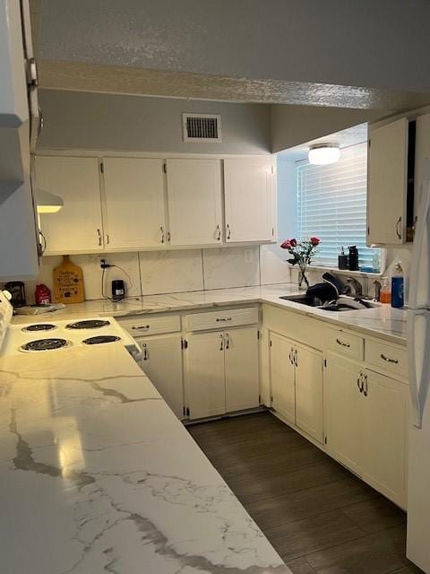 kitchen with dark wood-style floors, white cabinets, light stone countertops, visible vents, and a sink