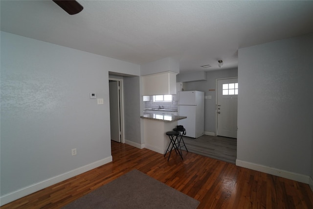 kitchen with baseboards, freestanding refrigerator, dark wood finished floors, white cabinetry, and decorative backsplash