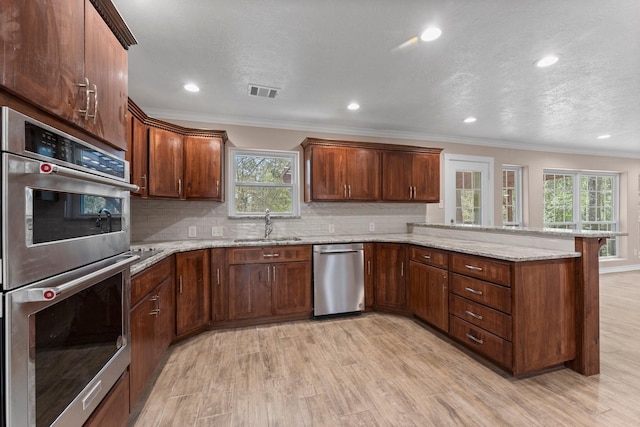 kitchen featuring light wood-type flooring, stainless steel appliances, a sink, visible vents, and a peninsula