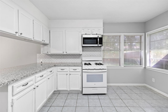 12109 22nd St, Santa Fe, TX 77510 - kitchen with stainless steel microwave, white gas range, decorative backsplash, light tile patterned floors, and white cabinets