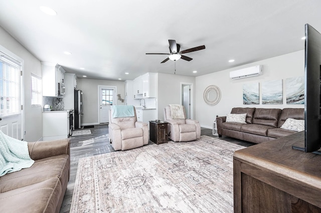 living area with ceiling fan, wood finished floors, a wall unit AC, and recessed lighting