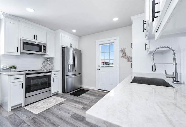 kitchen featuring white cabinetry, a sink, stainless steel appliances, and light wood-type flooring