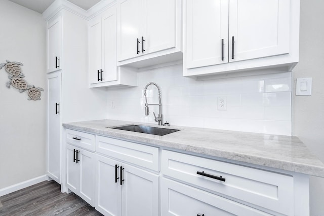 kitchen with decorative backsplash, light stone countertops, dark wood-type flooring, white cabinetry, and a sink