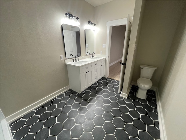 bathroom featuring double vanity, toilet, baseboards, and a sink