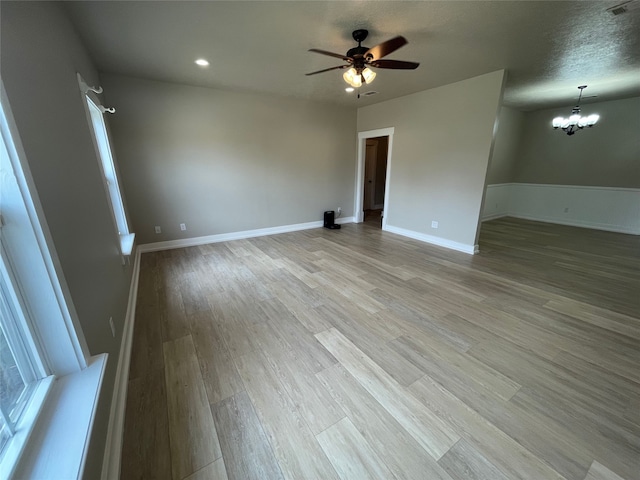 unfurnished room with light wood finished floors, ceiling fan with notable chandelier, visible vents, and baseboards