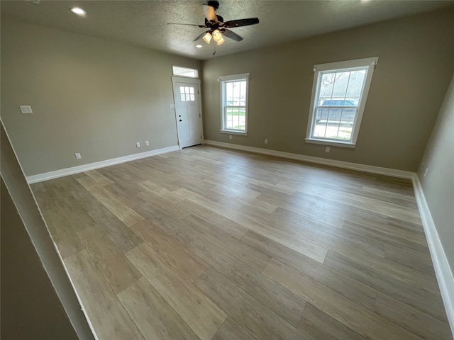 spare room with a ceiling fan, baseboards, light wood finished floors, and a textured ceiling