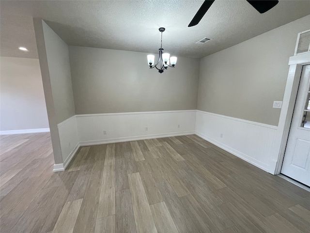 empty room with wood finished floors, a textured ceiling, wainscoting, ceiling fan with notable chandelier, and visible vents