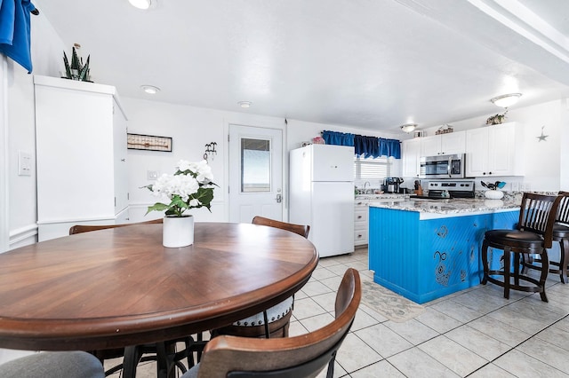 kitchen with light tile patterned floors, a breakfast bar area, white cabinetry, appliances with stainless steel finishes, and a peninsula
