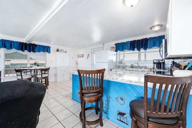 kitchen with light tile patterned floors, a peninsula, freestanding refrigerator, and beam ceiling