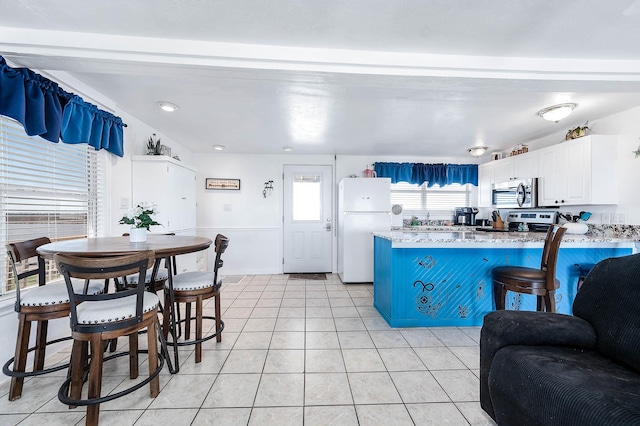 kitchen with freestanding refrigerator, stainless steel microwave, white cabinetry, a peninsula, and light tile patterned flooring