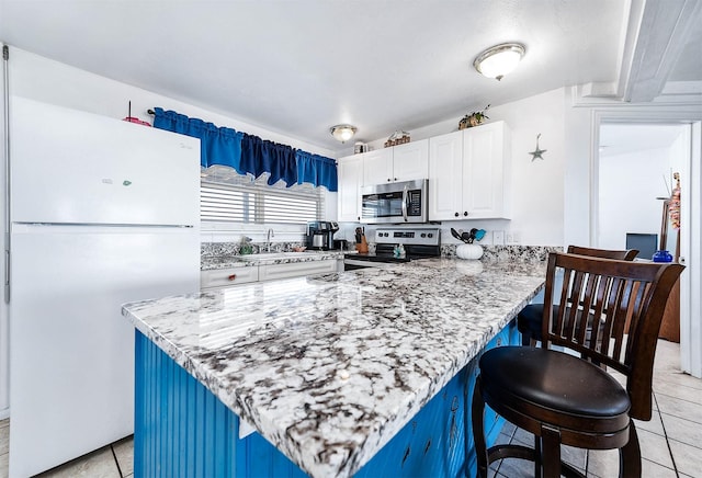 kitchen featuring appliances with stainless steel finishes, a sink, white cabinetry, a peninsula, and a kitchen breakfast bar