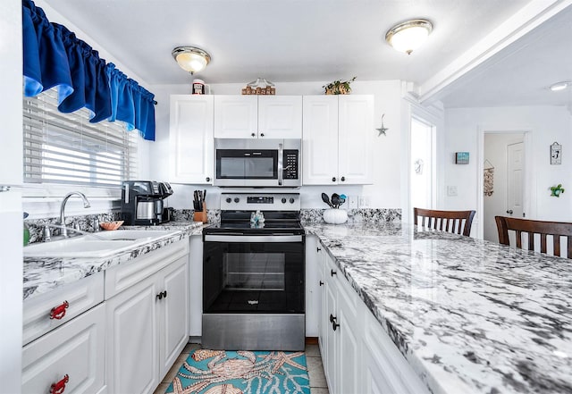 kitchen featuring white cabinets, stainless steel appliances, light stone countertops, and a sink