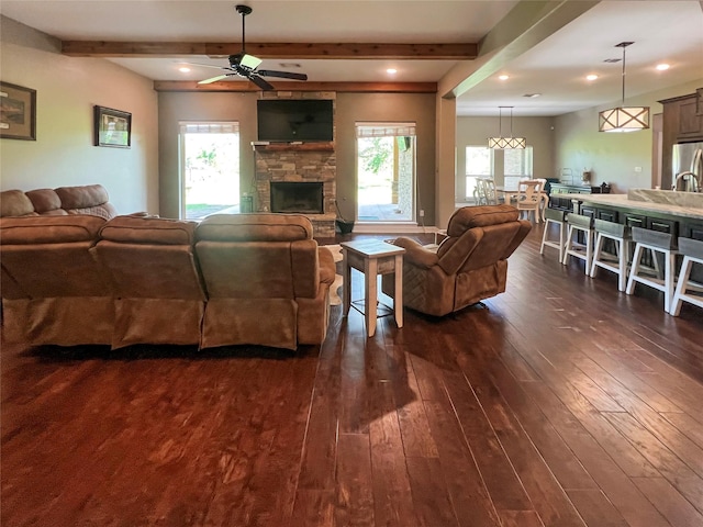 living room with beamed ceiling, a healthy amount of sunlight, a ceiling fan, and dark wood finished floors