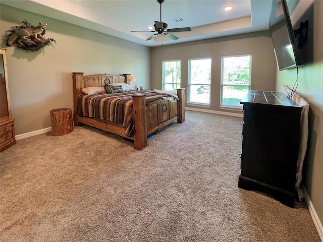 carpeted bedroom with visible vents, baseboards, a raised ceiling, and a ceiling fan