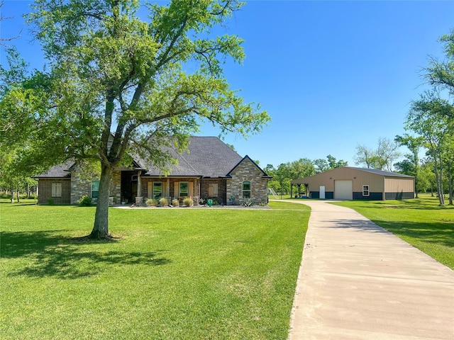 view of front of home featuring a front yard, an outdoor structure, stone siding, and a detached garage