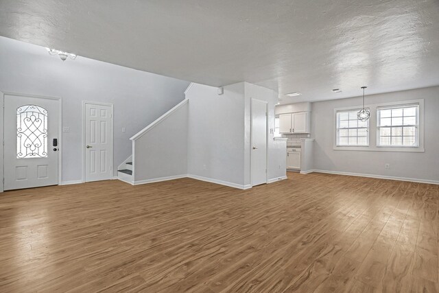 6802 Prairie Village Dr, Katy, TX 77449 - unfurnished living room featuring a textured ceiling, baseboards, light wood finished floors, and stairs