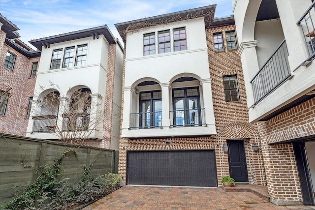 view of front facade with stucco siding, decorative driveway, brick siding, and an attached garage
