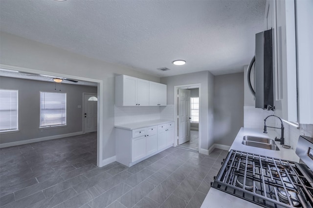 kitchen with tasteful backsplash, a sink, light countertops, white cabinets, and visible vents
