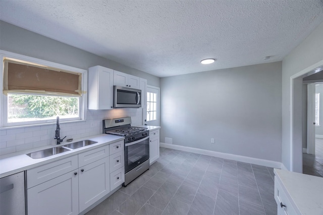 kitchen with white cabinets, light countertops, a sink, tasteful backsplash, and appliances with stainless steel finishes