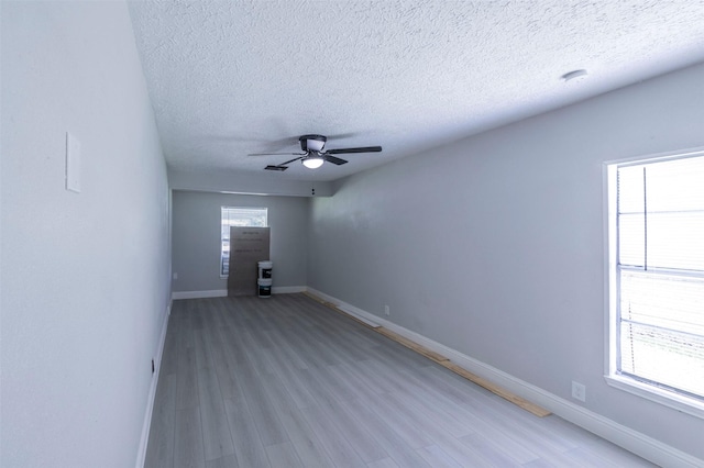 unfurnished room with a textured ceiling, light wood finished floors, baseboards, and a ceiling fan