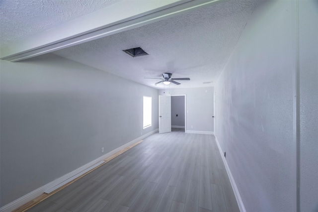 empty room with baseboards, a ceiling fan, wood finished floors, and a textured ceiling